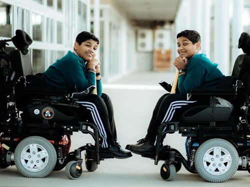 Sri Lankan twin boys in wheelchairs resting their chins on a cricket bat
