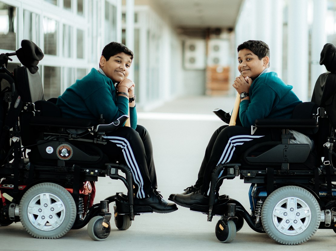 Twin Sri Lankan boys in wheelchairs resting their chins on a cricket bat.jpg