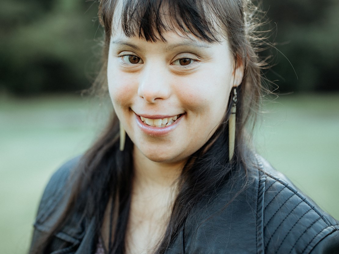 A confident looking and smiling young woman with Down Syndrome wearing black leather jacket