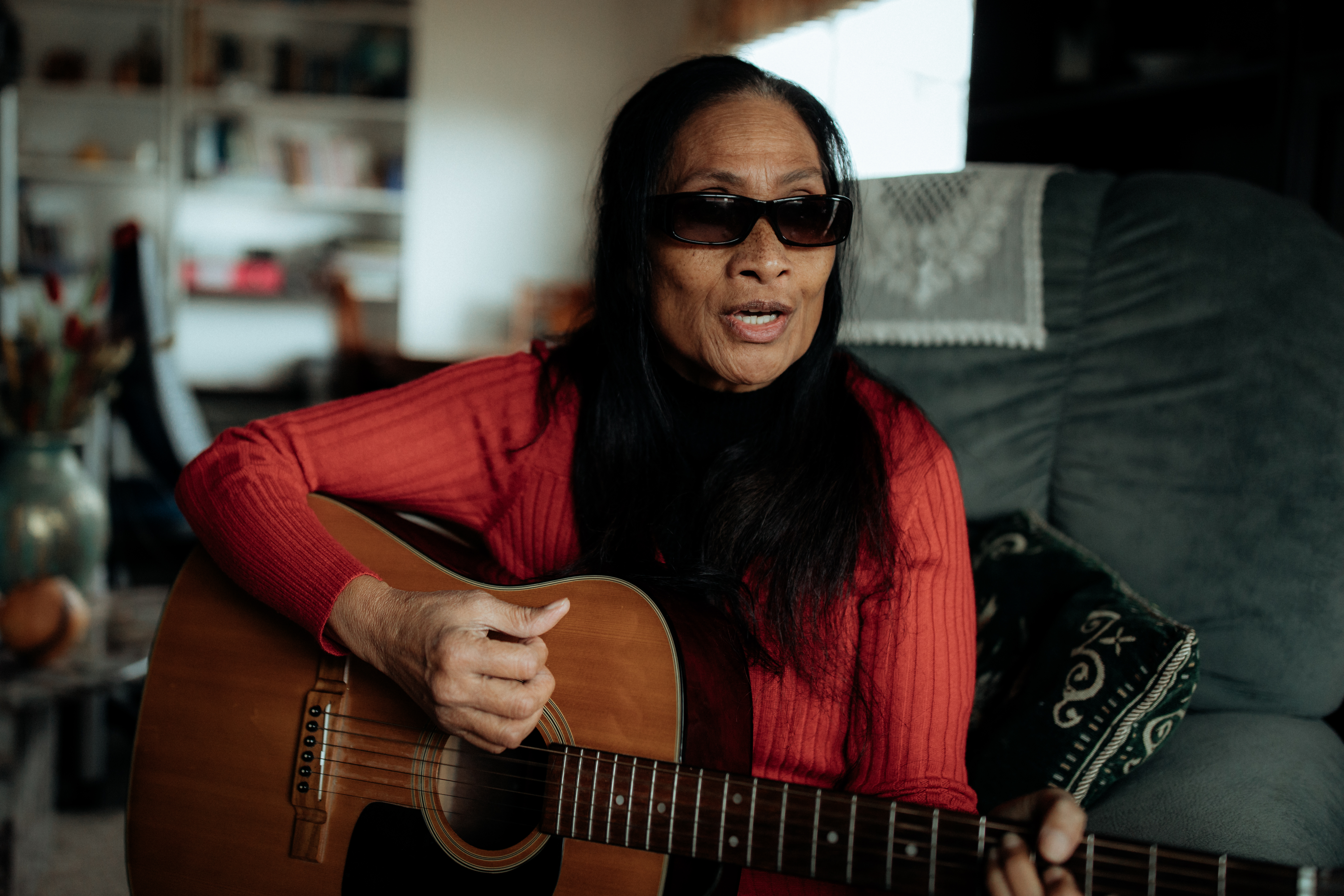 A middle aged Pasifica woman with vision impairment playing a guitar