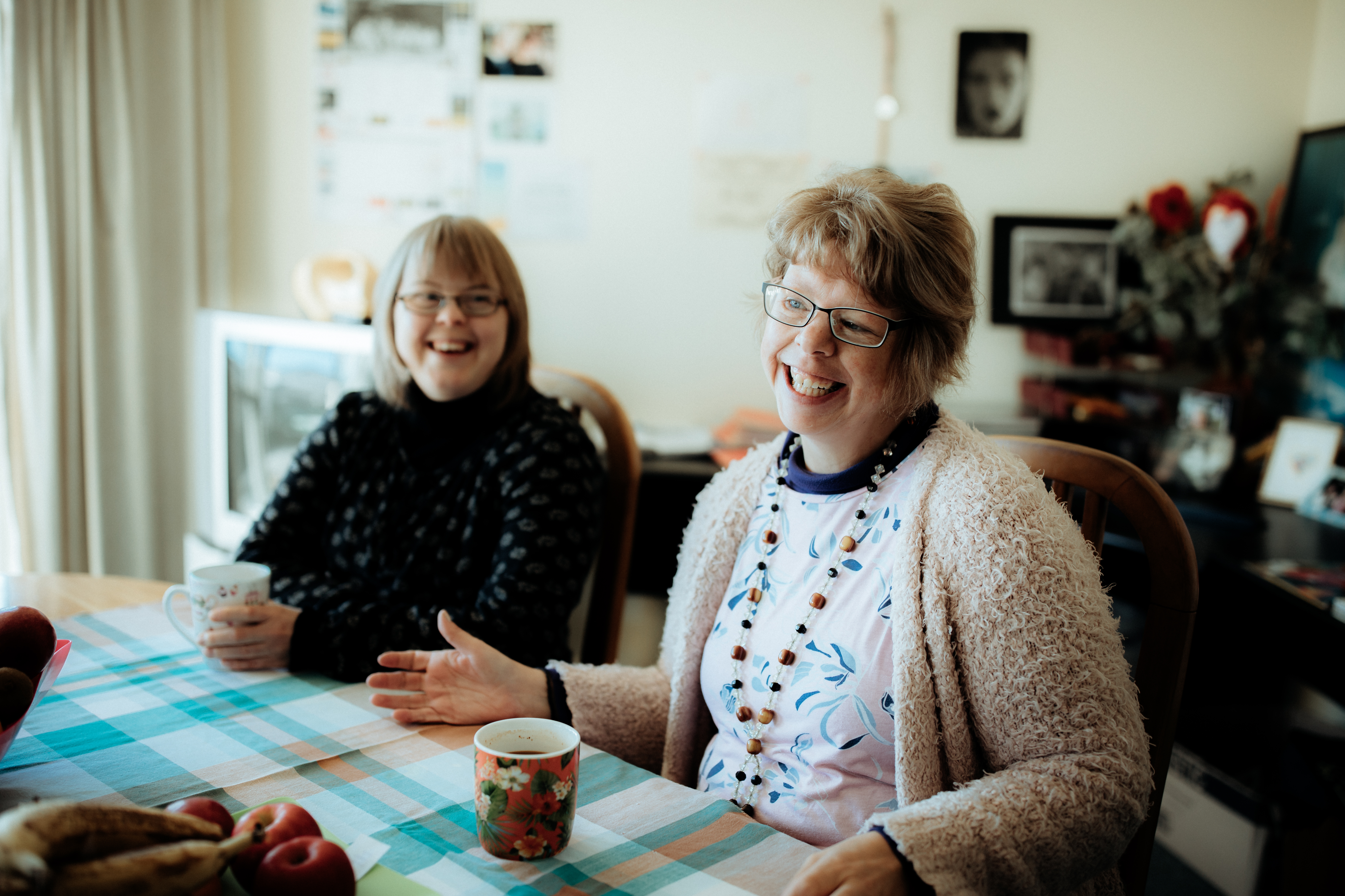 Adult women flatmates with intellectual disability smiling brightly and enjoying a cuppa