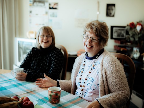 Adult women flatmates with intellectual disability smiling brightly and enjoying a cuppa