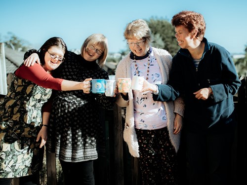 A group of female flatmates with intellectual disability happily clinking tea cups on the deck on a sunny day.jpg