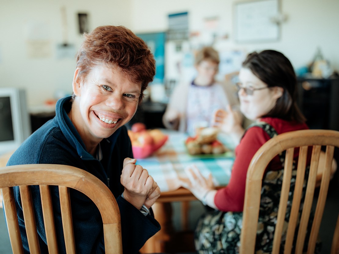 Smiling woman with intellectual disability and her flatmates in the background